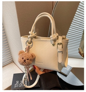 Detail of cream woven bucket bag with knot handles, shoulder strap and plush bear charm