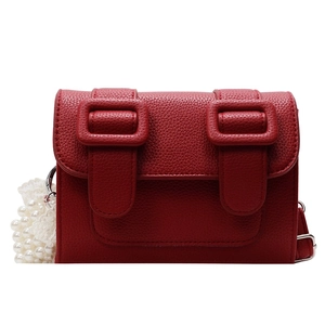 Red pebbled leather crossbody bag with dual buckles and decorative pearl lace chain