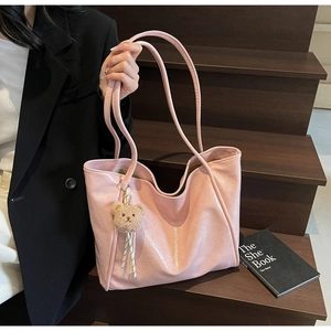 Detail of pink oil wax leather tote bag with brown plush bear charm on wooden steps