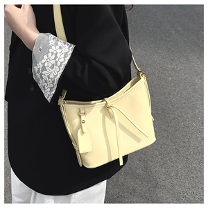Détail d'un sac seau en cuir ciré crème avec sangle décorative sur un blazer noir