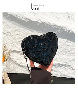 Close-up of black heart-shaped crossbody bag with embossed patterns and silver chain strap