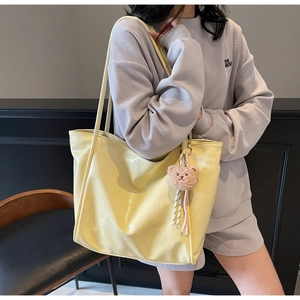 Detailed close-up of glossy yellow faux leather tote bag with brown bear plush keychain