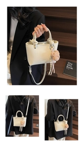 Close-up of white woven bucket bag with logo, bear charm and adjustable strap
