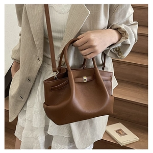 Detailed close-up of brown pebbled leather bucket bag with a metal lock on wood stairs