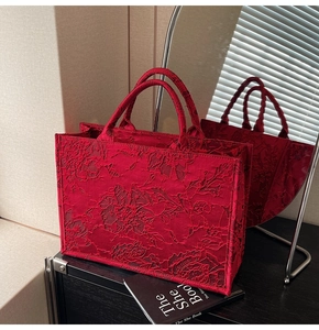 Detailed view of red bridal tote bag with floral embroidery on an elegant black surface