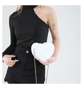Detail of white heart-shaped crossbody bag with embossed patterns and silver chain strap