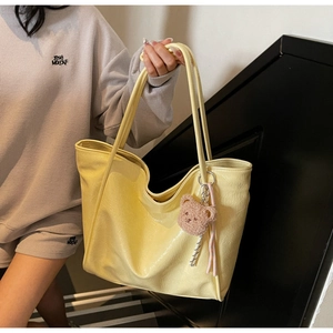Detail of glossy yellow leather tote bag with cute bear charm and woven rope decoration