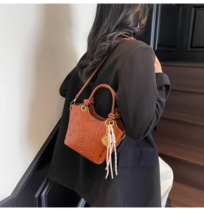 Close-up of brown bucket bag with cartoon embossing, tassels, and knotted handles