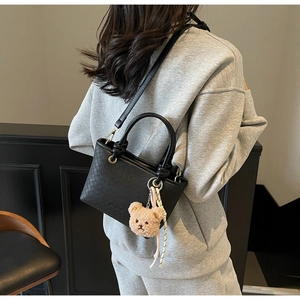Detail of black woven bucket bag with cute bear charm and ribbon on grey sweatshirt