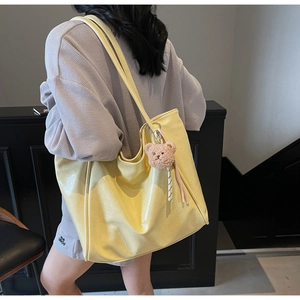Detailed side view of yellow wax leather tote bag with plush bear charm on shoulder