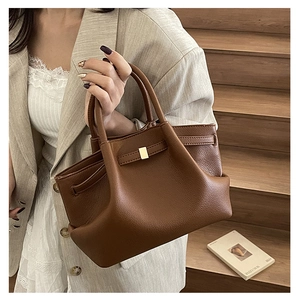Detailed close-up of brown lychee leather texture and golden metal buckle on bucket bag