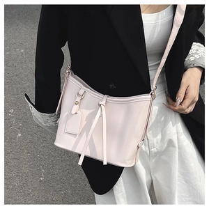 Détail d'un sac seau en cuir ciré rose avec bandoulière à nœuds porté sur tenue chic