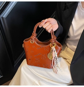 Detail of brown embossed bucket bag with cute motifs and tennis racket pendant
