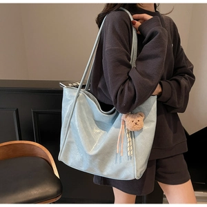 Detail of light blue oil wax leather tote bag with glossy texture and teddy bear charm