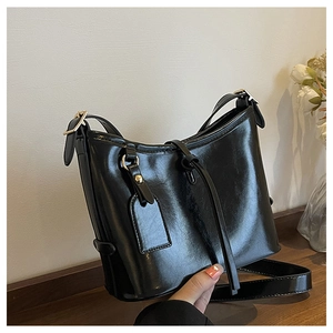Détail d'un sac hobo noir brillant avec boucle dorée et bandoulière tenu à la main