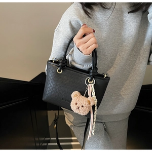 Detail of black woven bucket bag with cute plush bear charm and striped ribbon accent