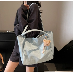 Close-up of light blue oil wax leather tote bag with a cute plush bear charm detail