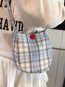 Blue and white plaid crossbody egg bag with a red button shown on a casual female model