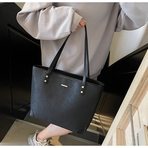 Detail of black woven texture tote bag with golden logo plaque and reinforced corners