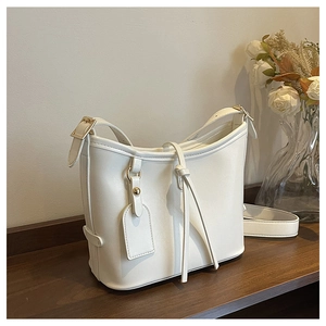 Vue détaillée du sac seau blanc en cuir huilé avec boucles dorées sur plateau en bois