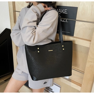Detail view of woven texture black tote bag with gold studs on a shoulder strap