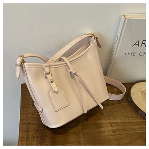 Détail d'un sac seau en cuir verni blanc crème posé sur une table en bois décorée