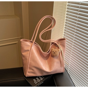 Pink faux leather tote bag with cute bear charm and tassel detail on dark leather surface
