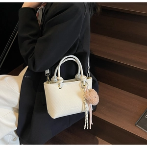 Detail of white embossed bucket bag with plush bear charm and Meigefei logo on stairs