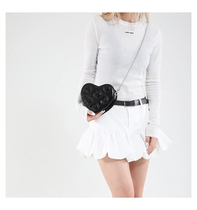 Detail of black heart-shaped crossbody bag with quilted stitching and silver chain strap