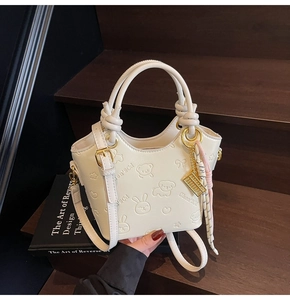 Detail of cream bucket bag with cartoon embossed leather texture and gold hardware charms