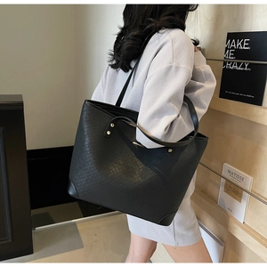 Detail of black woven textured tote bag with gold rivets and long shoulder handles