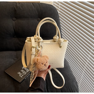 Close-up of beige woven bucket bag with knot handle detail and cute bear charm