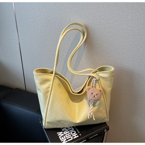 Detail of soft cream faux leather tote bag with brown plush bear charm on books