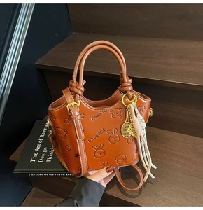 Detail shot of brown embossed bucket bag with cartoon patterns and tennis racket charm