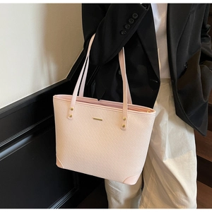 Detail of light pink tote bag featuring woven texture and gold metal hardware accents