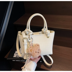 Close-up of a white woven bucket bag featuring knotted handles and a brown plush bear charm
