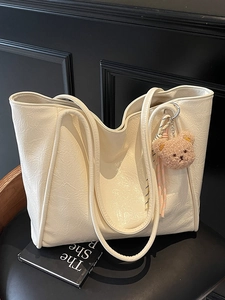 Cream-colored oil wax leather tote bag with a plush bear charm on a dark chair