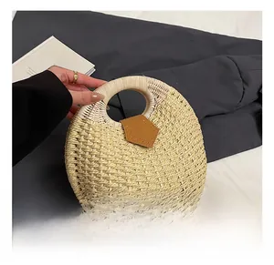 Detail showing hand-held woven straw handbag with round handle and leather patch