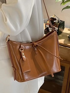 Sac seau chic en cuir ciré marron caramel porté avec un blazer blanc style rétro chic