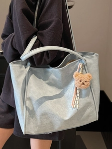 Light blue faux leather tote bag with a small plush bear charm worn by a model