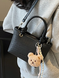 Minimalist black woven bucket bag with a cute plush bear pendant and adjustable strap