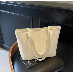 Detail shot of a cream woven tote bag with gold hardware on a leather chair