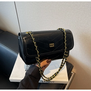 Detail of black quilted leather crossbody bag with V-shaped stitching and gold chain