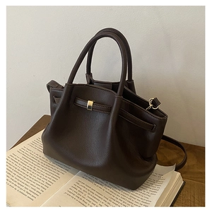 Close-up of dark brown lychee leather bucket bag with gold buckle detail on a book