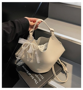 Detail view of beige lychee texture bucket bag with elegant pearl lace bow charm