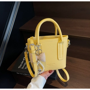 Detailansicht gelbe Eimer-Handtasche mit Litschi-Muster, Schleife und Perlenanhänger