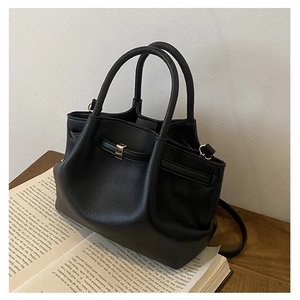 Detail of black lychee grain leather handbag with gold buckle and dual handles