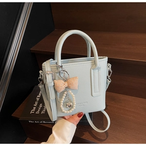 Detail der hellblauen Handtasche mit Litschi-Struktur und Perlenanhänger auf Holzstufen
