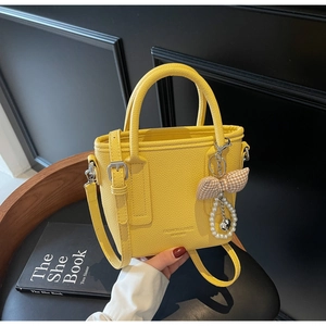 Detail der gelben Leder-Eimertasche mit Schleifenanhänger und geprägtem Logo