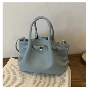 Detail of light blue textured bucket bag with gold buckle on open book background